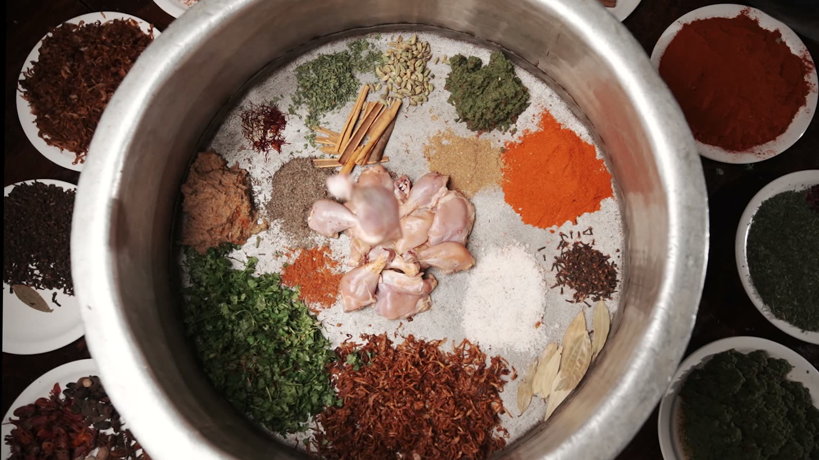 Chicken and a full set of ground spices laid out in an open steel handi
