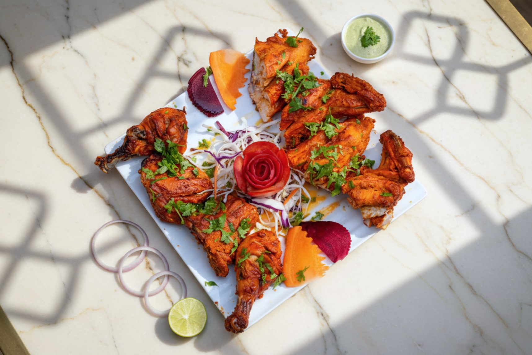 A whole tandoori chicken, charred at the edges, with onion and lime