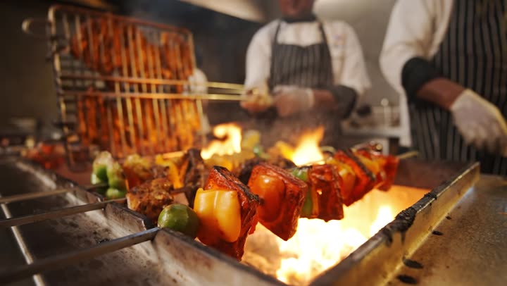 Chefs working chicken and vegetables over an open grill